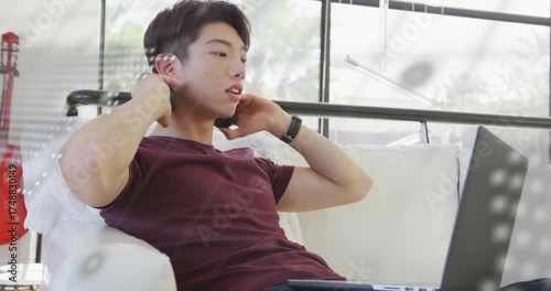 Technology student coding on couch and activating animated code overlay while adjusting headphones