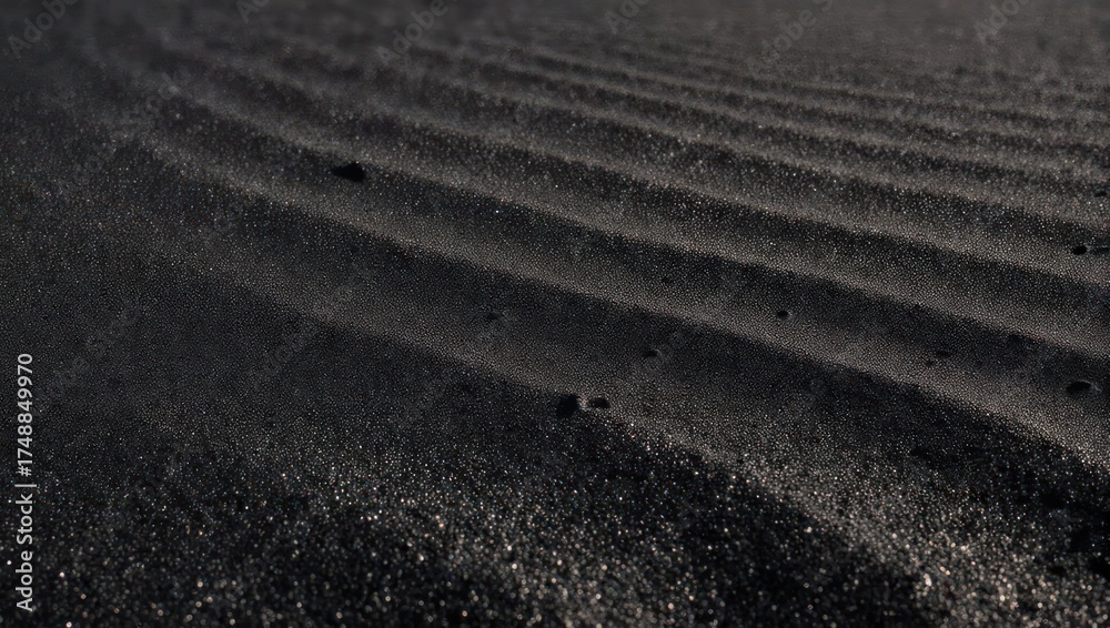 Naklejka premium Close-up shot reveals textured ripples in black sand, reflecting subtle light