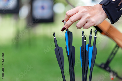 Close-up of a female archer's hand selecting or handling black and blue fletching arrows from a quiver.