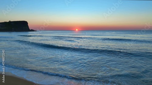 Soft waves roll ashore beneath a blush-toned sky, as the sun rises at Avalon Beach on Sydney’s Northern Beaches.