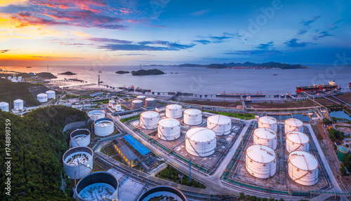 Massive coastal oil and gas terminal with white storage tanks at the port at dusk. Global trade and energy industry background.