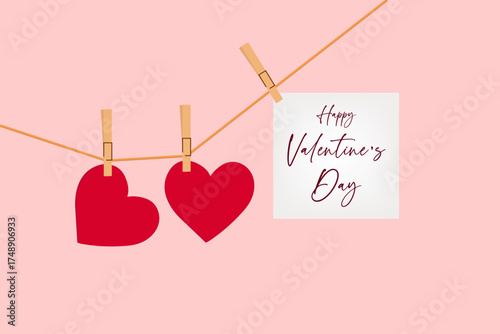 A pink background with two red hearts and a "Happy Valentine's Day" card hanging on a string with clothespins.