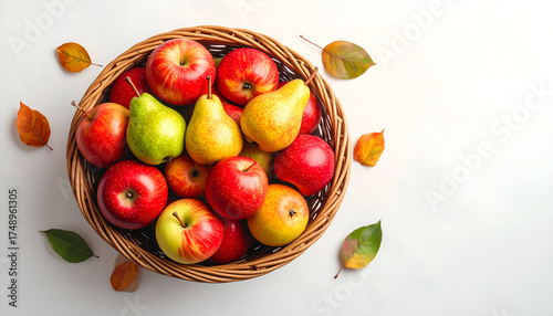 Freshly picked red apples and yellow pears in a rustic wicker basket, surrounded by autumn leaves on a white background.