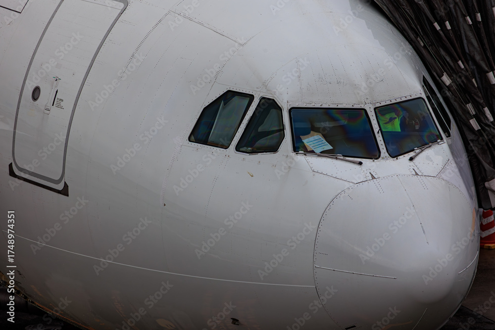 Obraz premium Close-up view of a commercial airplane cockpit and nose section at an airport. A pilot is preparing for flight, representing the aviation and travel industry.