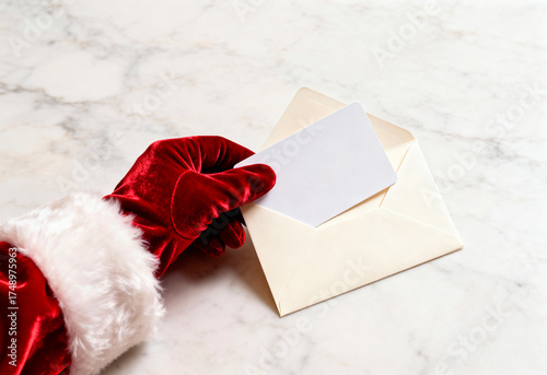 Santa glove sliding blank card into cream envelope on marble