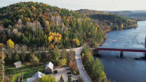 Aerial view of beautiful old red bridge and smooth green waters of a lake on a sunny autumn day. Bird's eye view of scenic emerald lake surrounded by forests and houses.