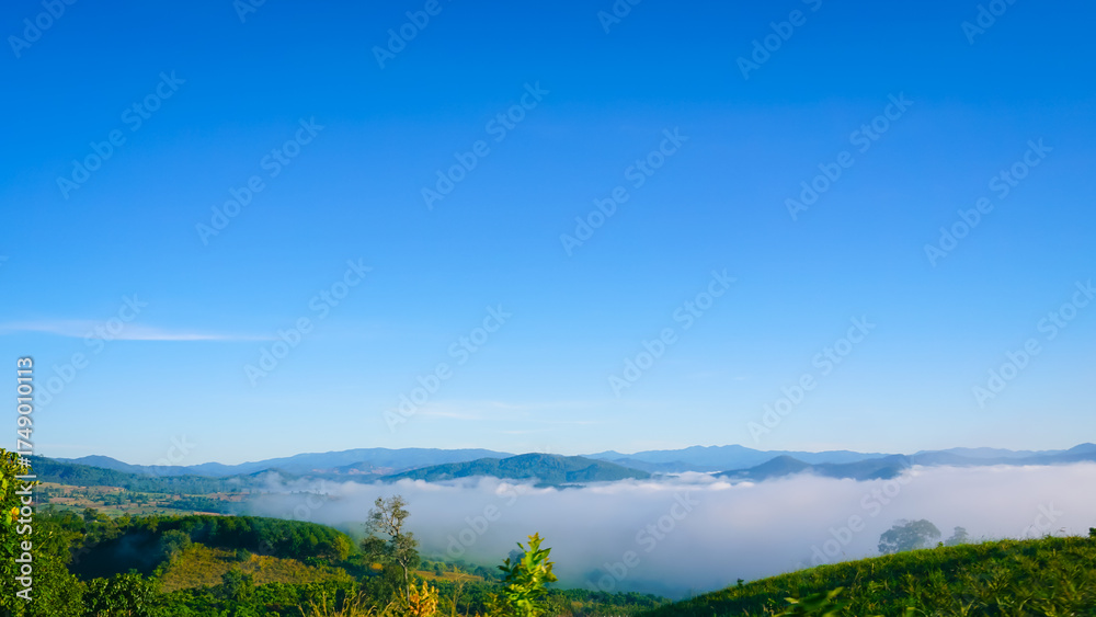 Fototapeta premium Beautiful mountain landscape with morning fog and clear blue sky. A scenic view of misty hills and lush greenery, perfect for nature, travel, environment, and outdoor adventure concepts.