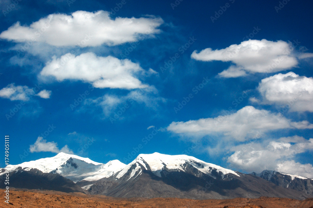 Fototapeta premium Snow-capped mountains under a clear blue sky with scattered clouds