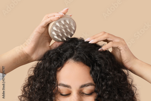 Photos Beautiful young African-American woman using scalp massager for her healthy curl