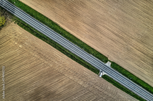Fototapeta Naklejka Na Ścianę i Meble -  Top-down aerial vertical shot of car on rural road through harvested fields in Mazury, Poland, summer bright light, drone stock image