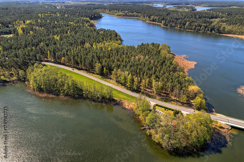 Fototapeta Naklejka Na Ścianę i Meble -  Vertical oblique aerial shot of narrow bridge spanning lake inlet with wooded shoreline, Mazury Poland summer, drone, daylight, commercial stock