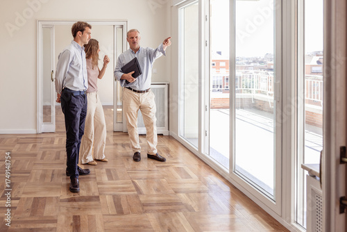 Estate agent showing a young couple the city views from an unfurnished house with a large balcony.