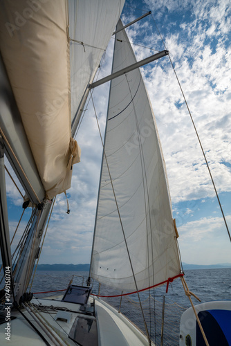 Full white sails blown by the wind against blue sky during sailing near Croatia. Symbol of movement, freedom and summer maritime journey.