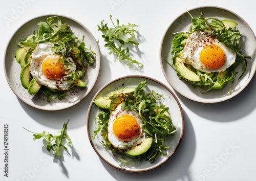 Three plates of fried eggs, avocado, and arugula