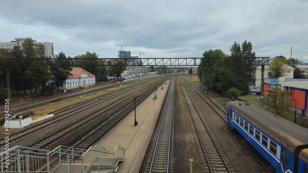 Naklejka premium Railway tracks with a blue train under a cloudy sky in urban area