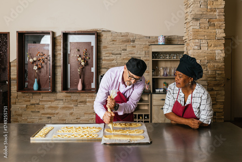 Experienced baker piping filling onto pastry dough while apprentice watches