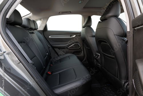 Backseat view of modern car interior with black leather seats, white stitching, geometric door accents and rubber mats