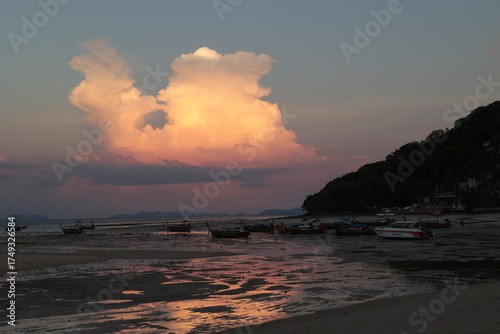 Fototapeta Dramatic sunset illuminating clouds over the empty seabed at low tide with boats
