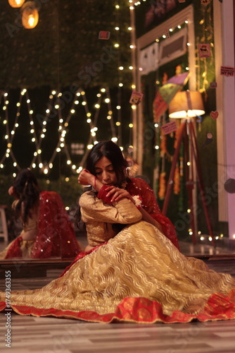 Portrait of an Indian Nepali woman wearing traditional red and golden lehenga sitting gracefully indoors with festive lights in background