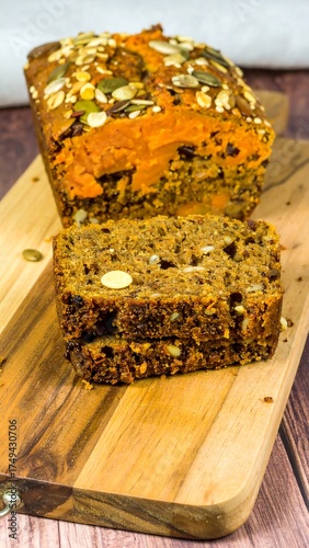 A loaf of bread, partially sliced, on a wooden cutting board. The bread is topped with seeds and grains