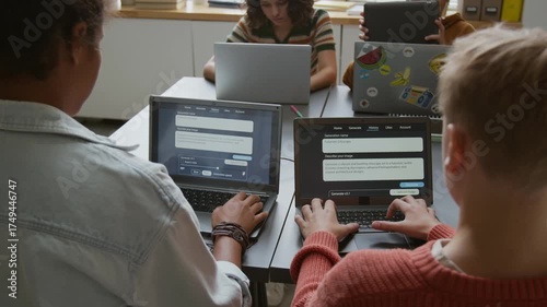 Medium rear shot of group of busy diverse young children sitting at desks in classroom at STEM lesson, writing prompts for AI image generator program on laptops, while working on projects