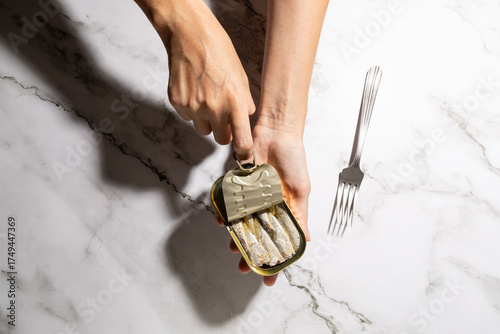 Female hands opening canned sardines on kitchen countertop