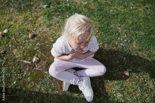 4 year old girl sitting on the grass making a painful grimace does not want to go anywhere