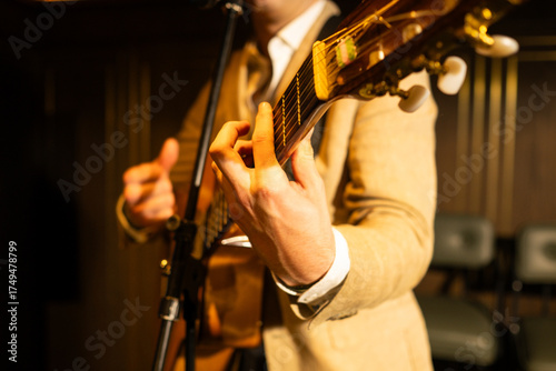 Close-up of a man playing acoustic guitar with microphone in front, on stage under warm light. Musical performance concept with focus on hands, instrument, and concert atmosphere.