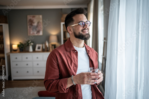 Foto Man in glasses holding water looking out window smiling