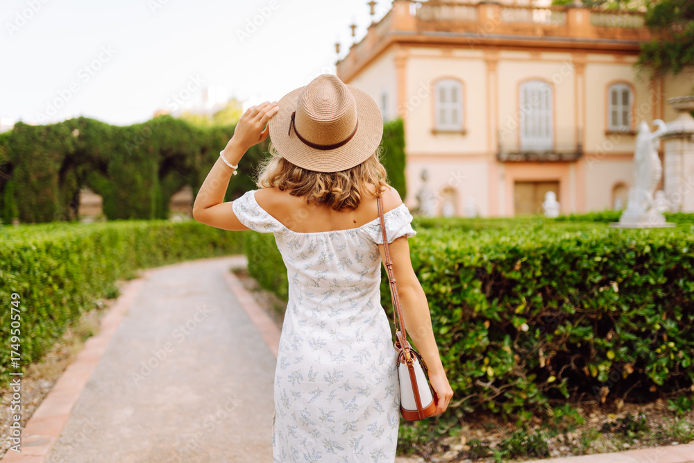 Fototapeta premium Young woman in a summer dress enjoying the sunshine in a beautiful garden setting during the late afternoon
