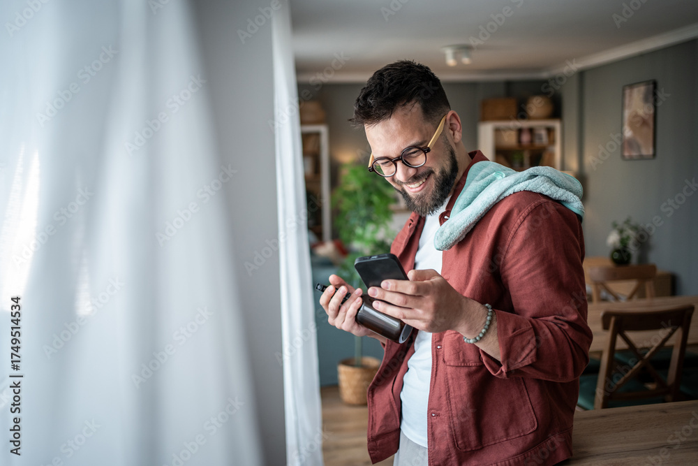 Fototapeta premium Smiling man using phone and holding vape device indoors
