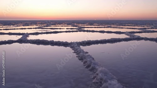 sunrise colorful - A serene salt flat landscape at dusk, reflecting pastel hues of pink and orange in the calm water, with salt crusts forming geometric patterns across the surface