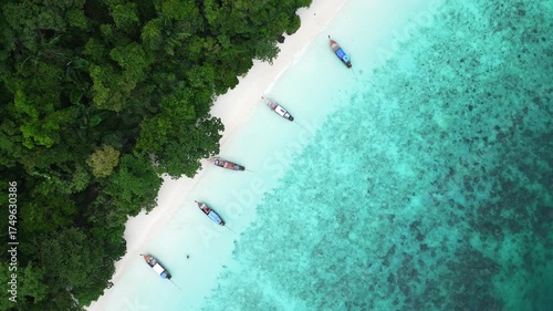 Aerial view of Monkey Beach on Ko Phi Phi Island, Thailand, showing turquoise sea, white sandy beach, tropical jungle and traditional long tail boats anchored near the shore.