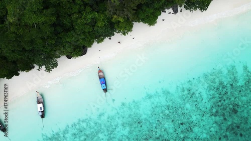 Aerial view of Monkey Beach on Ko Phi Phi Island, Thailand, showing turquoise sea, white sandy beach, tropical jungle and traditional long tail boats anchored near the shore.