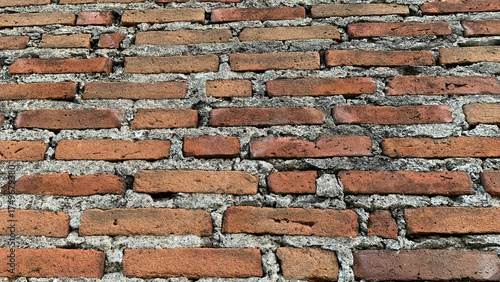 Detailed background texture of an aged and weathered wall constructed from traditional orange-red clay bricks set in rough gray cement mortar. Construction concept