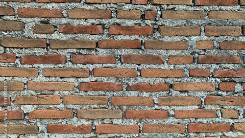 Detailed background texture of an aged and weathered wall constructed from traditional orange-red clay bricks set in rough gray cement mortar. Construction concept
