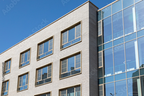 Modern building facade with brick and glass panels under blue sky. Clean architectural lines for commercial or residential projects. Real photo