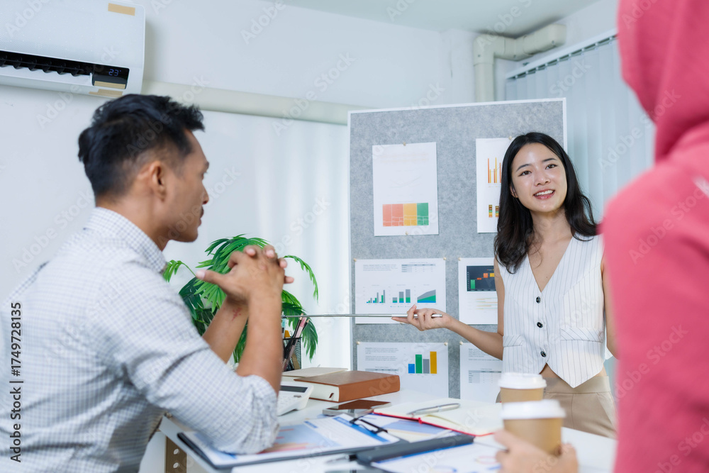 Fototapeta premium A woman and a man are talking in front of a white board with a picture on it. The woman is pointing at the picture and the man is looking at her 