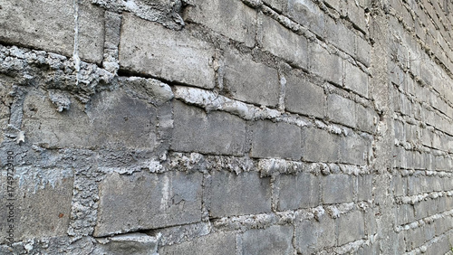 Detailed side-angle view of a weathered exterior wall constructed from rough gray concrete cinder blocks joined by thick, unevenly textured white mortar. Construction concept