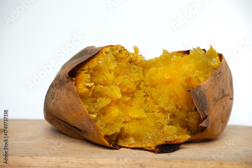 Golden-yellow roasted Ubi Cilembu sweet potato split open on wood surface, highlighting its caramelized texture and natural sweetness.