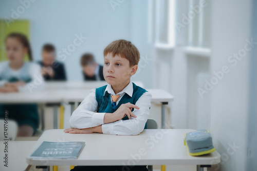8 years old boy wearning green uniform vest and white shirt sitting at the class in school.
