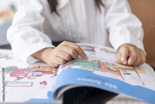 Child Reading Book with Colorful Illustrations in Bright Studio Light Focus on Child's Hands and Open Book with Foreground and Background Elements