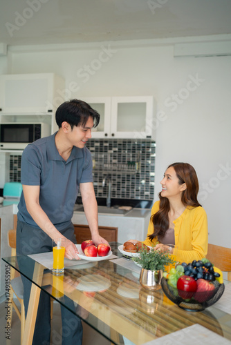 Young Asian couple prepare healthy breakfast at modern home kitchen sharing happy morning meal moment eating fresh fruit togetherness bonding daily life
