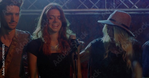 Singing bandmates on stage near metal truss, holding microphone and playing guitar under lights