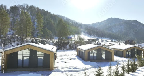 Cluster of small cottages rests quietly on snowy slope. Scene highlights rustic design alpine hospitality and winter calm. Winter chalet