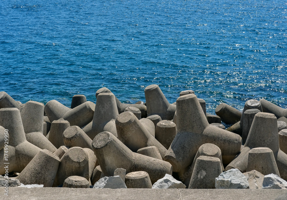 Obraz premium Close-up view of interlocking concrete tetrapods forming a breakwater against the sparkling blue sea.