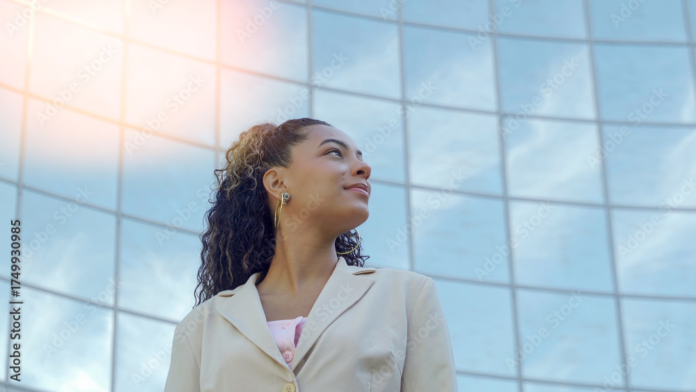 Obraz premium Young businesswoman looking up with a visionary expression in front of a modern glass building