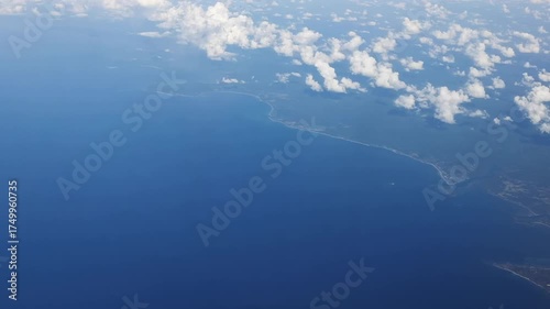 A breathtaking aerial view reveals the deep blue ocean and land beneath drifting clouds.