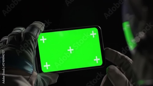 Hands in Gloves Holding a Green Screen Smartphone in a Dark, Mysterious Environment