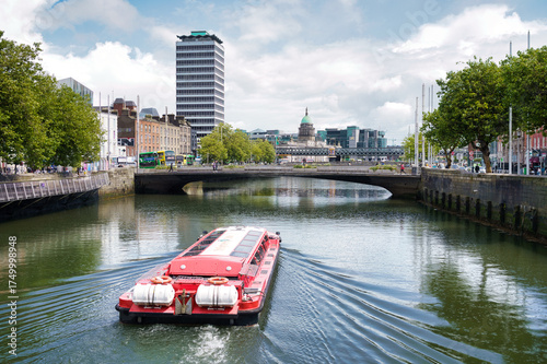 Photography A vibrant shot of Dublin, Ireland, capturing the River Liffey with a tourist boat, bridges, and cityscapes under a bright sky